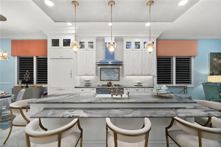 Kitchen with tasteful backsplash, decorative light fixtures, a kitchen breakfast bar, white cabinets, and wall chimney exhaust hood