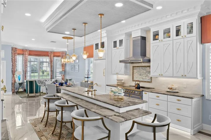 Kitchen featuring a center island with sink, white cabinets, wall chimney exhaust hood, hanging light fixtures, and stone counters