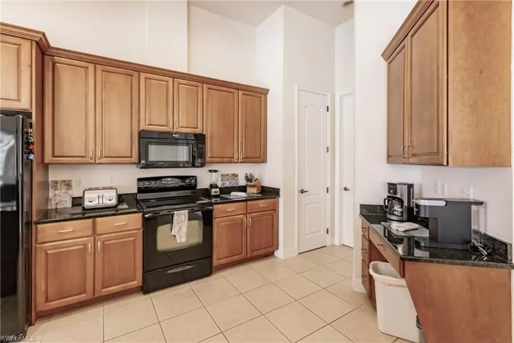 Kitchen featuring a high ceiling, light tile patterned floors, black appliances, and dark stone countertops