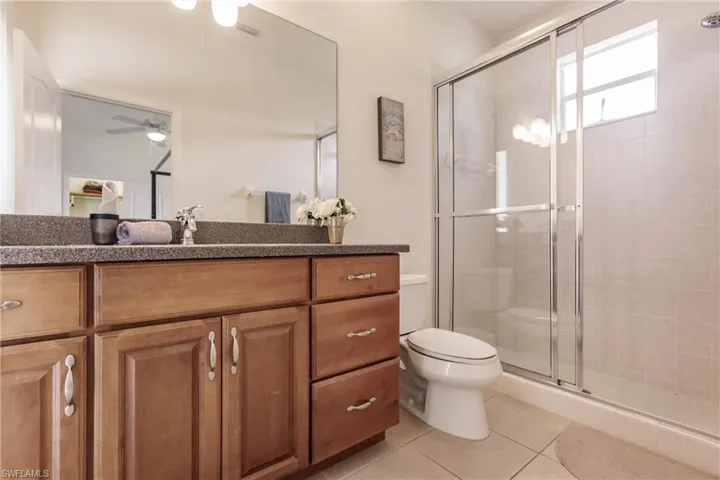 Bathroom featuring tile patterned floors, a shower with door, vanity, toilet, and ceiling fan
