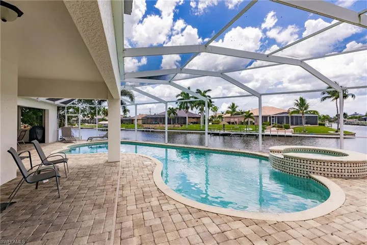 View of pool with a lanai, a water view, a patio, and an in ground hot tub