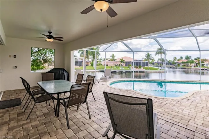 View of pool with a lanai, ceiling fan, a patio area, and a water view