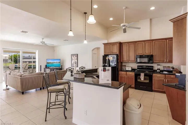 Kitchen featuring black appliances, a kitchen bar, decorative light fixtures, ceiling fan, and light tile patterned floors