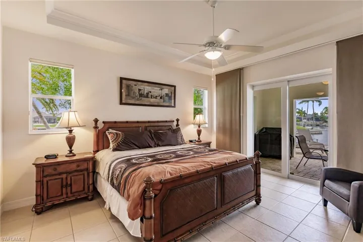 Bedroom with light tile patterned floors, ceiling fan, access to exterior, and a tray ceiling