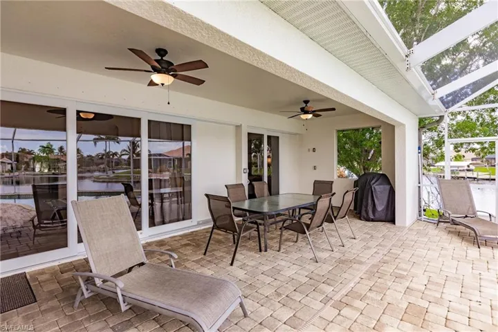 View of patio with glass enclosure, grilling area, a water view, and ceiling fan
