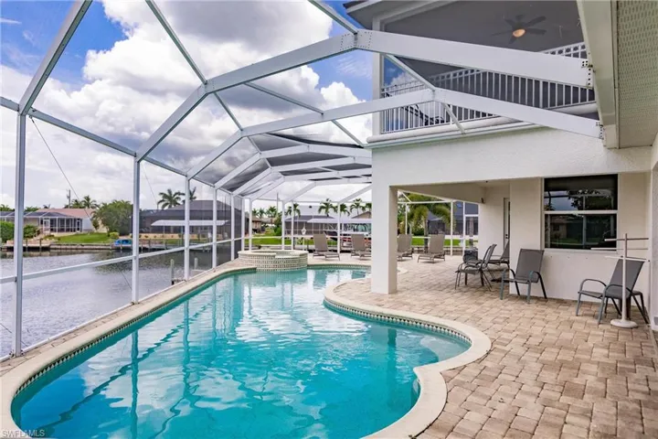 View of pool featuring a patio area, an in ground hot tub, glass enclosure, and a water view
