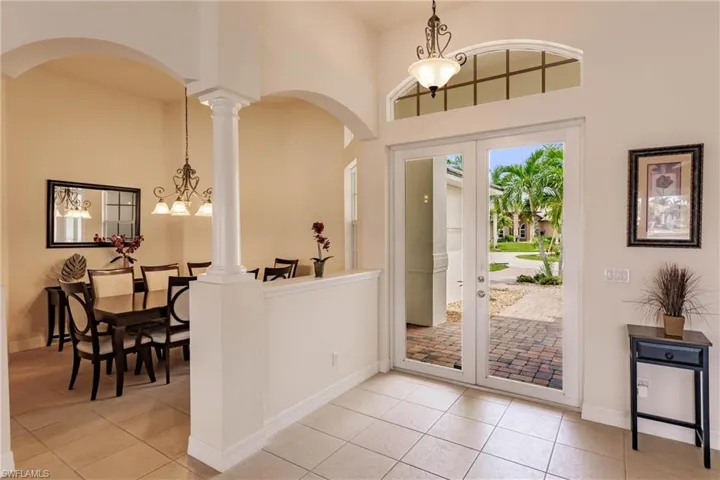 Entryway featuring light tile patterned floors, french doors, a chandelier, and decorative columns