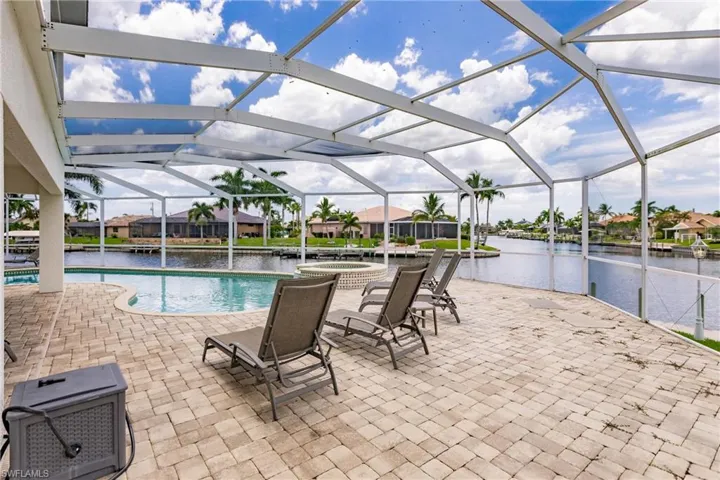 View of pool featuring a patio area, an in ground hot tub, pool water feature, glass enclosure, and a water view