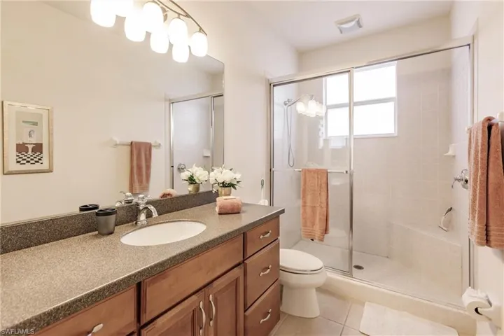 Bathroom featuring walk in shower, vanity, tile patterned floors, and toilet