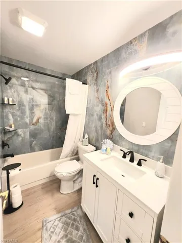 Full guest bathroom with hardwood / wood-style flooring, vanity, toilet, and shower / bath combination with curtain