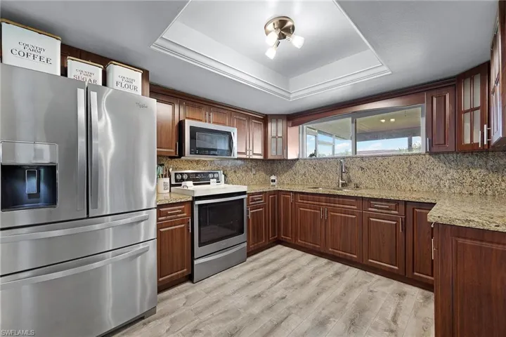 Kitchen featuring appliances with stainless steel finishes, a raised ceiling, sink, and granite countertops