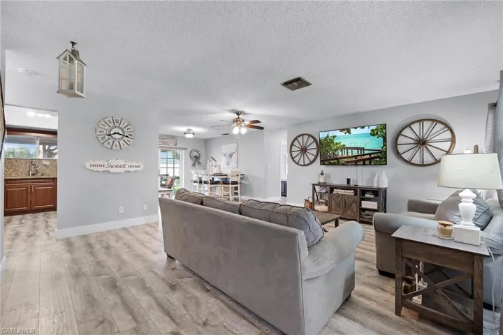 Living room with a textured ceiling, ceiling fan, sink, and light wood-type flooring