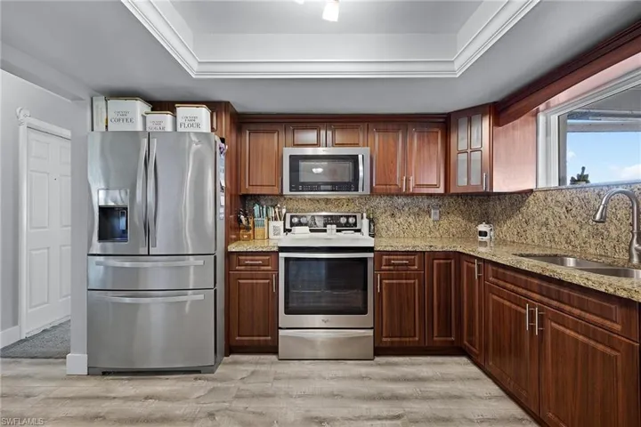 Kitchen featuring light wood-type flooring, tasteful backsplash, stainless steel appliances, sink, and light stone countertops