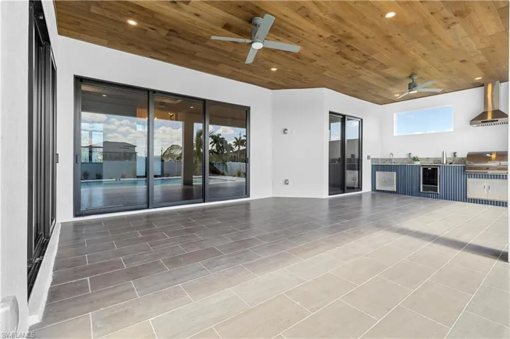 The covered patio features a flat wooden ceiling, an outdoor kitchen, and impact-resistant doors connecting to the living room, formal dining, and master suite.