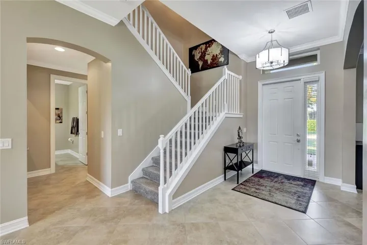 Foyer entrance with ornamental molding, a notable chandelier, and light tile patterned floors