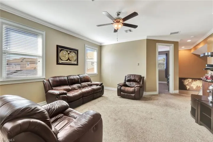 Carpeted living room featuring ornamental molding and ceiling fan