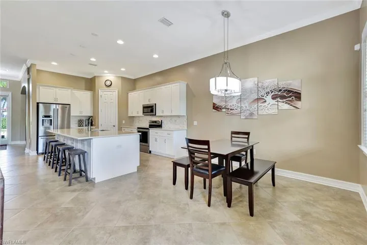 Kitchen featuring a center island with sink, stainless steel appliances, white cabinets, decorative light fixtures, and tasteful backsplash