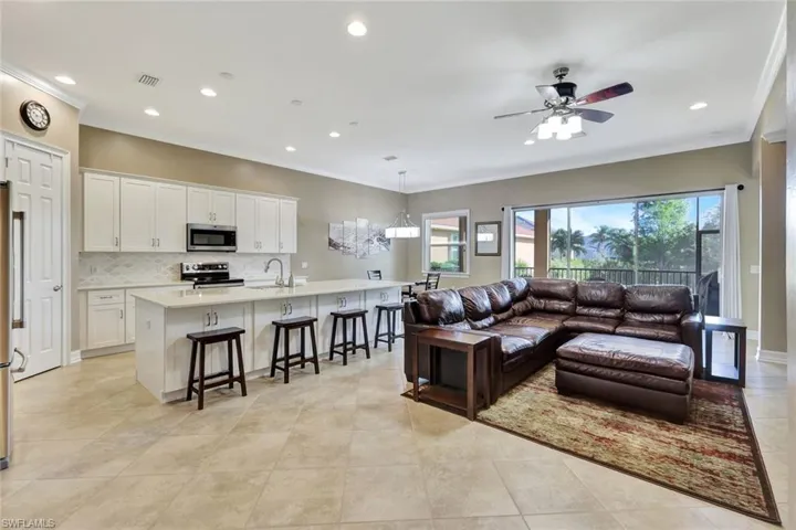 Living room with ceiling fan, light tile patterned flooring, crown molding, and sink