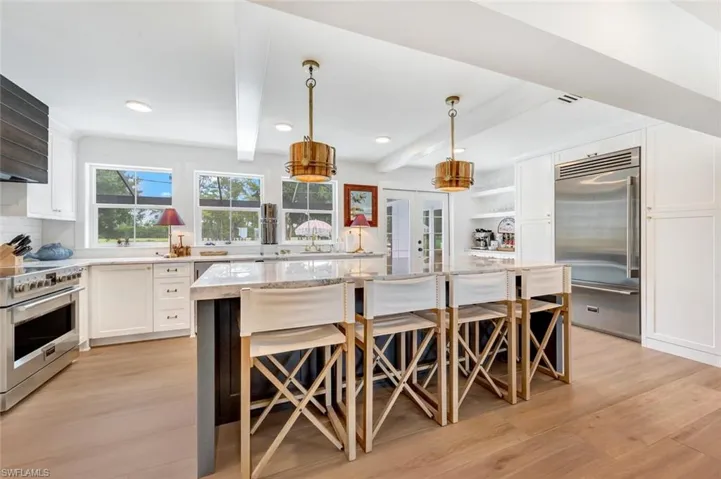Kitchen featuring white cabinetry, a kitchen island, light stone countertops, decorative light fixtures, and beamed ceiling