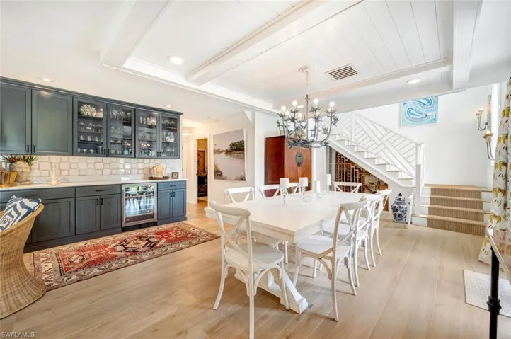 Dining room featuring stairway, light wood-style flooring, beverage cooler, a chandelier, and a wooden ceiling with exposed beams