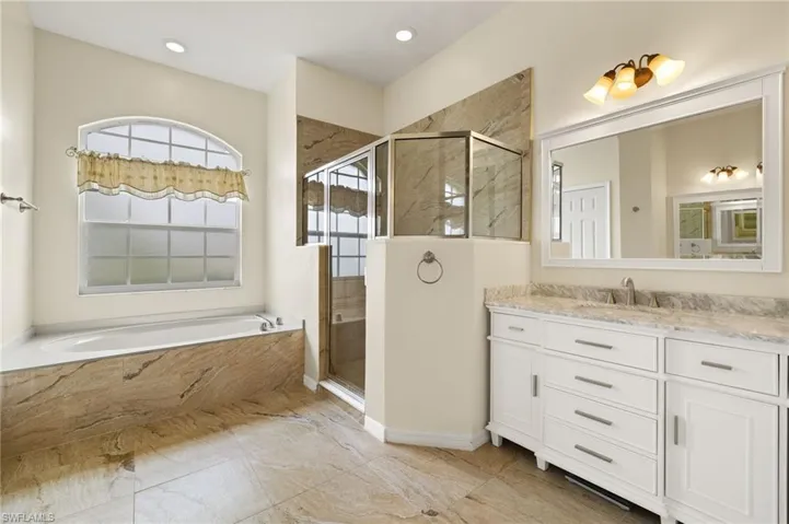 Bathroom featuring vanity, a marble finish shower, a bath, and recessed lighting