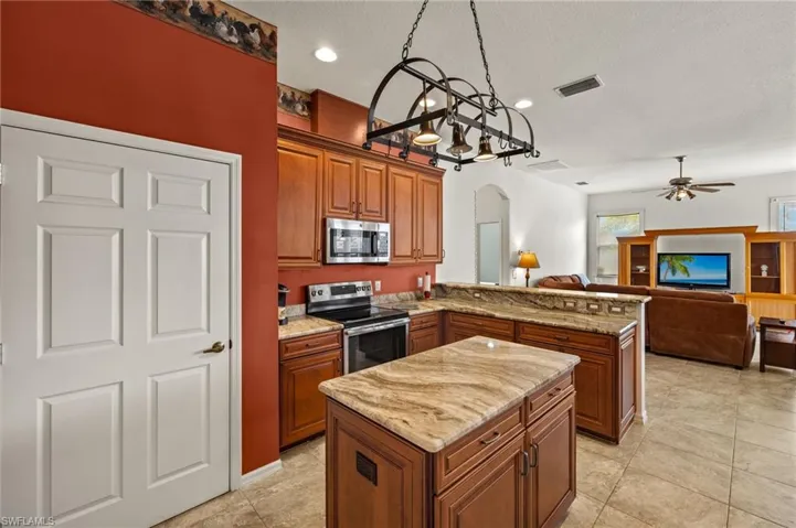 Kitchen featuring arched walkways, brown cabinets, stainless steel appliances, a peninsula, and light stone counters