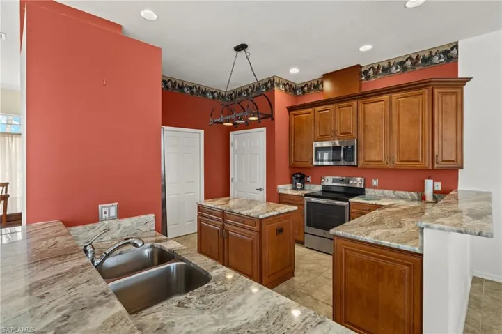 Kitchen with brown cabinets, a peninsula, stainless steel appliances, recessed lighting, and light stone countertops