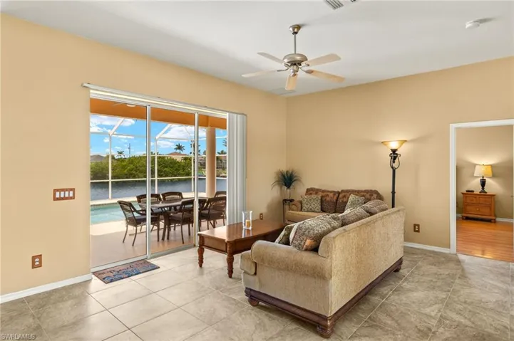 Living room with a sunroom, a water view, a ceiling fan, and light tile patterned floors