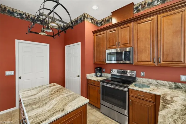 Kitchen with stainless steel appliances, brown cabinetry, light stone counters, and recessed lighting