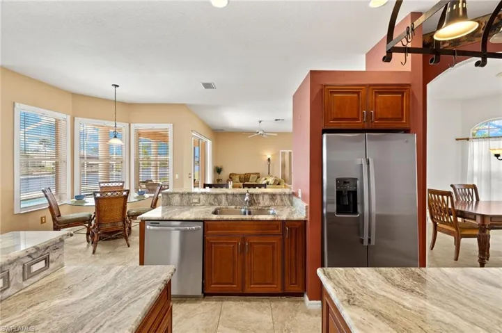 Kitchen with brown cabinets, light stone counters, appliances with stainless steel finishes, and decorative light fixtures