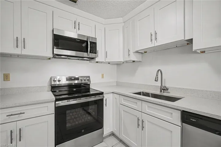 Kitchen featuring white shaker cabinetry, stainless steel appliances, light-toned countertops, and a stainless steel sink with a pull-down faucet