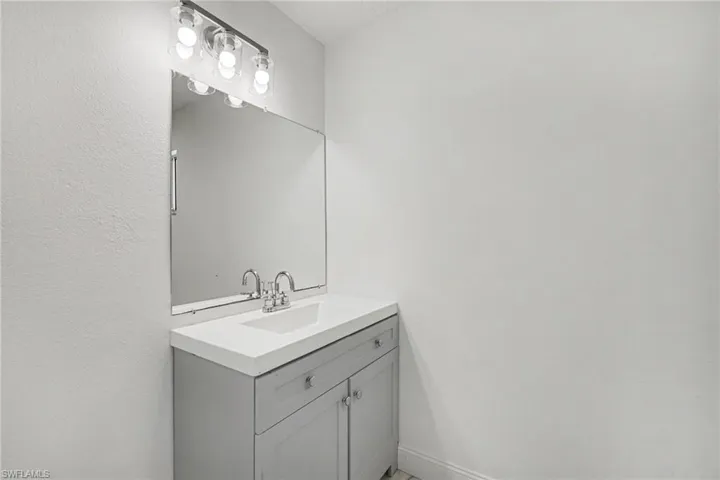 Vanity with integrated sink, chrome faucet, wall-mounted mirror, and overhead lighting fixture