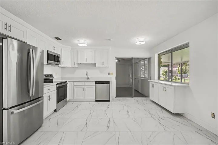 Kitchen featuring white cabinetry, stainless steel appliances, white countertops, and large format tile flooring