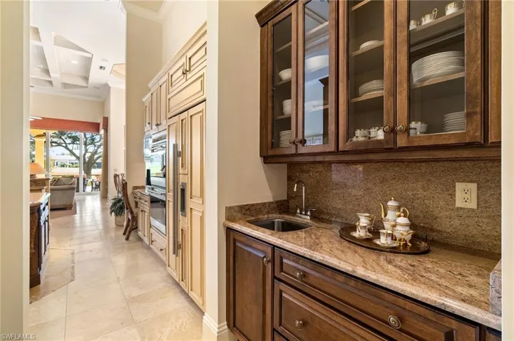 Bar with sink, ornamental molding, light stone countertops, decorative backsplash, and stainless steel oven