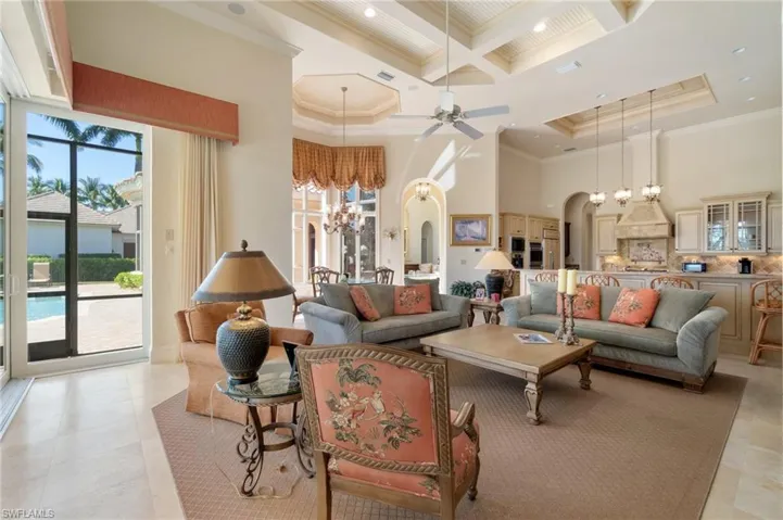 Living room featuring coffered ceiling, ornamental molding, a towering ceiling, beam ceiling, and ceiling fan with notable chandelier