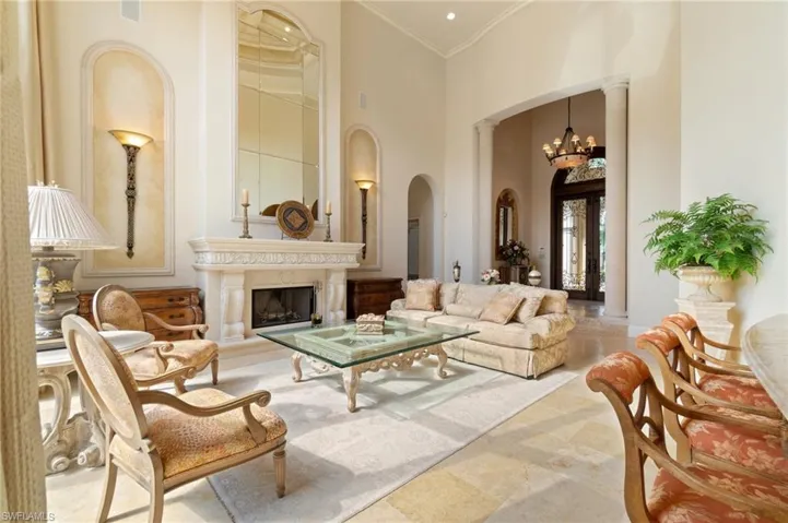 Living room with ornate columns, a chandelier, ornamental molding, a towering ceiling, and a high end fireplace