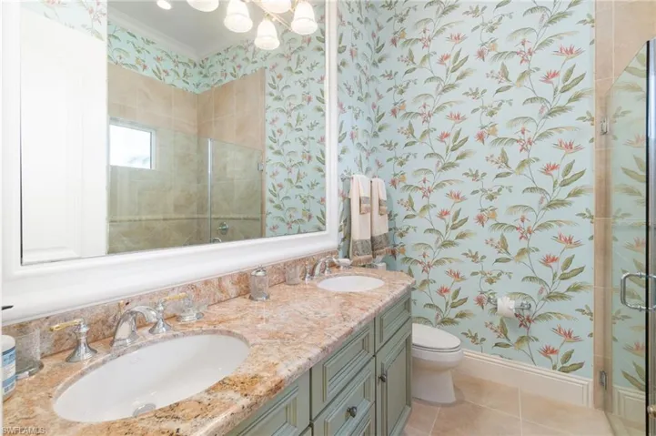 Bathroom with tile patterned floors, toilet, crown molding, vanity, and a shower with door