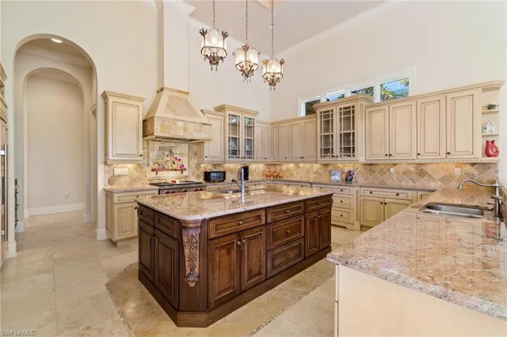 Kitchen featuring pendant lighting, sink, dark brown cabinetry, cream cabinets, and light stone counters