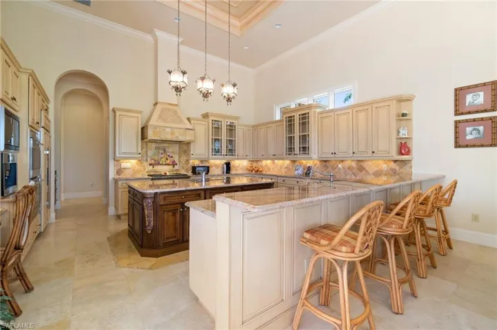 Kitchen featuring a kitchen breakfast bar, hanging light fixtures, ornamental molding, light stone counters, and kitchen peninsula