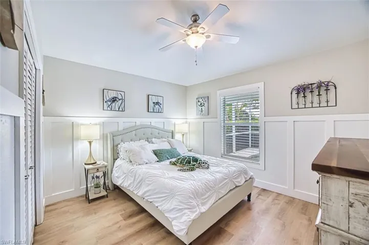 Bedroom with a decorative wall, a wainscoted wall, light wood-style floors, and a ceiling fan