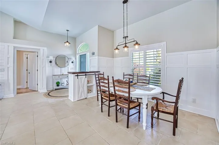 Dining room with a decorative wall, a wainscoted wall, light tile patterned floors, and vaulted ceiling