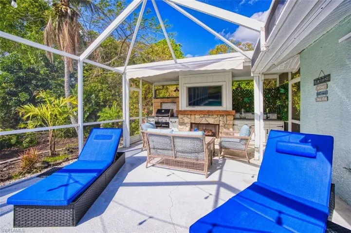 View of patio featuring a lanai, a sunroom, an outdoor stone fireplace, and an outdoor kitchen with living area