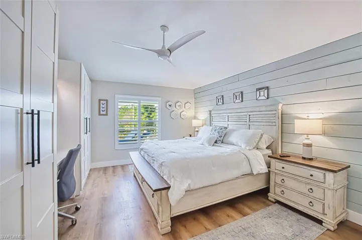 Bedroom with light wood-style flooring, a ceiling fan, wooden walls, and an office area