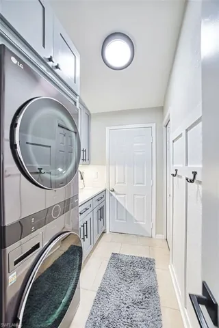 Laundry room featuring stacked washer / drying machine, light tile patterned floors, and cabinet space