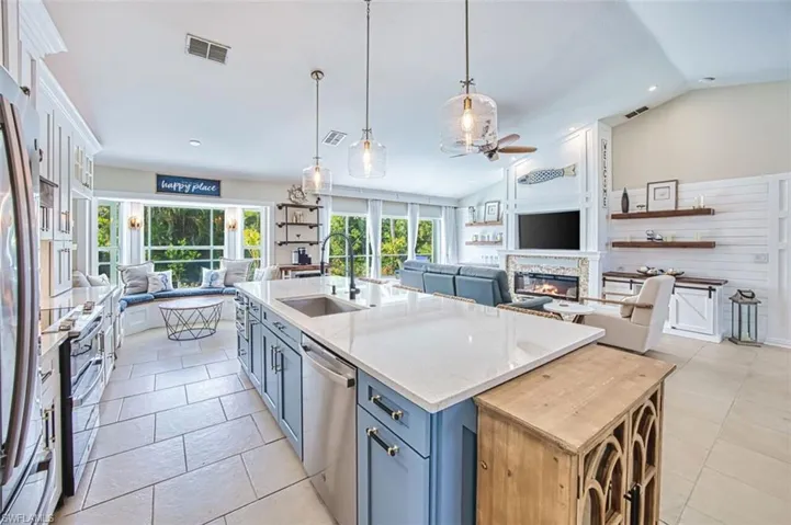 Kitchen featuring open floor plan, light stone counters, ceiling fan, a center island with sink, and a glass covered fireplace