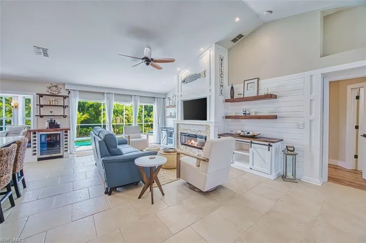 Living area with a glass covered fireplace, ceiling fan, recessed lighting, vaulted ceiling, and beverage cooler