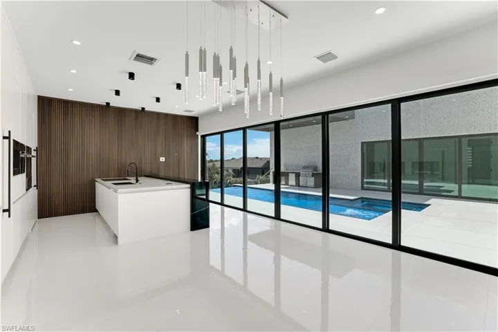 Kitchen with an island with sink, light tile patterned floors, a sink, modern cabinets, and decorative light fixtures