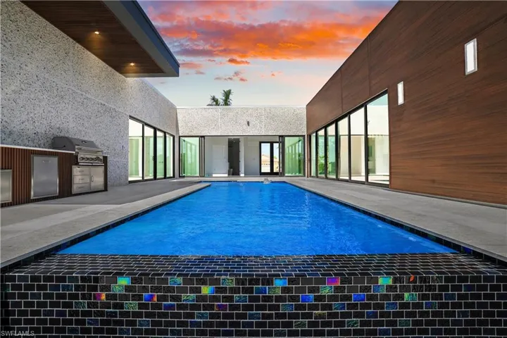 Pool at dusk with an outdoor kitchen, an outdoor pool, area for grilling, and a patio