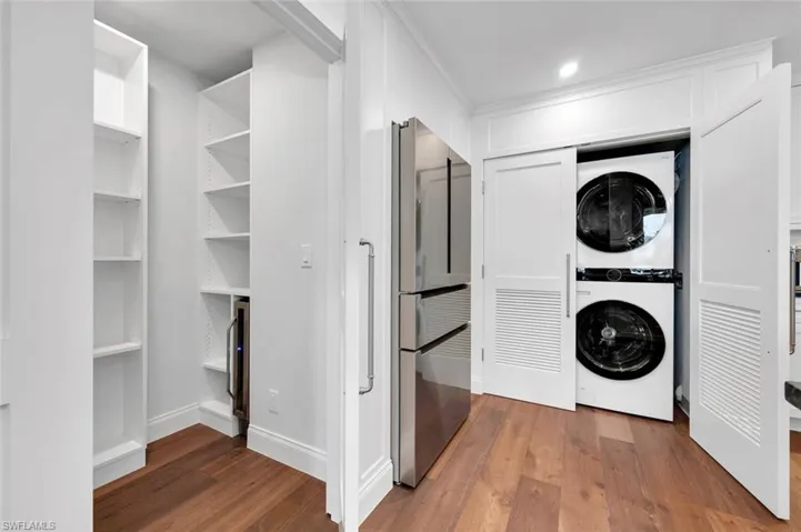 Washroom featuring dark wood-type flooring, estacked washer and dryer, and recessed lighting