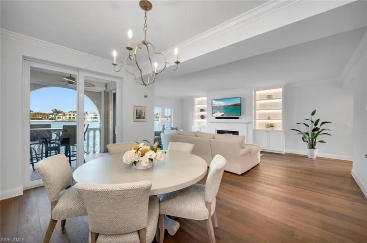 Dining room with ornamental molding, a lit fireplace, built in features, hardwood / wood-style floors, and a water view